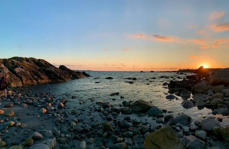 people stand on the rocks near the ocean as the sun sets