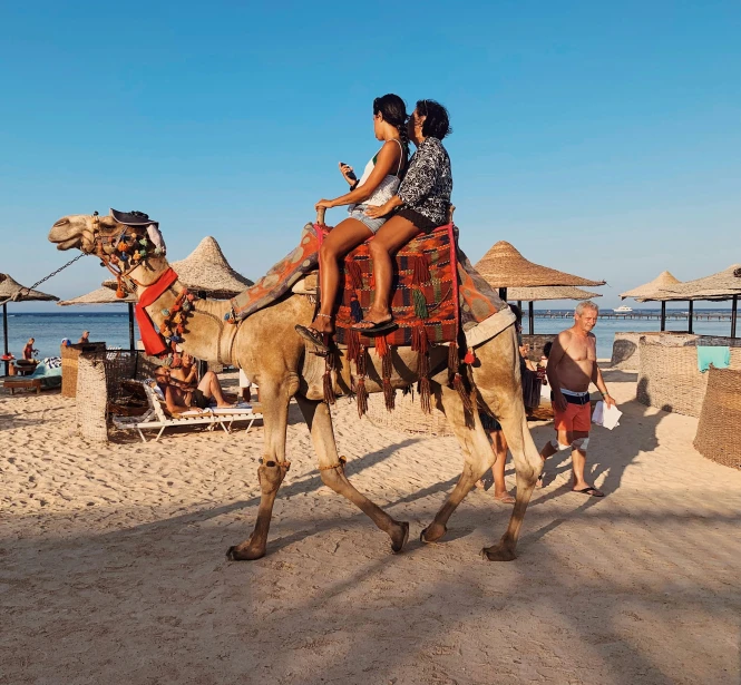 two women riding on top of a camel in the sand