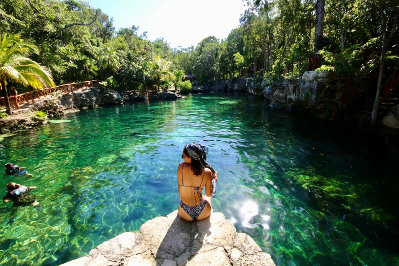 a woman in a short swimsuit standing on a rock near a river