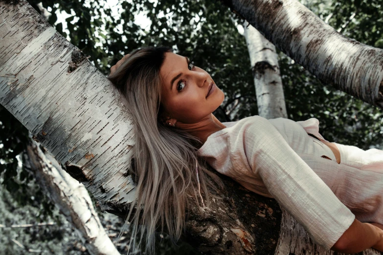 a young woman poses for a po, leaning up against a tree