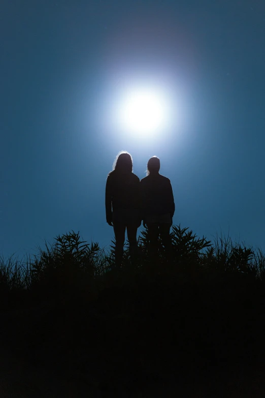 a man and woman standing at the top of a hill under a sunlit sky