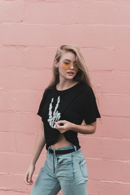 a woman wearing sunglasses standing in front of a pink brick wall