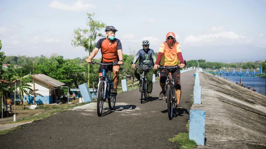 three bicyclists ride down an empty road near the water