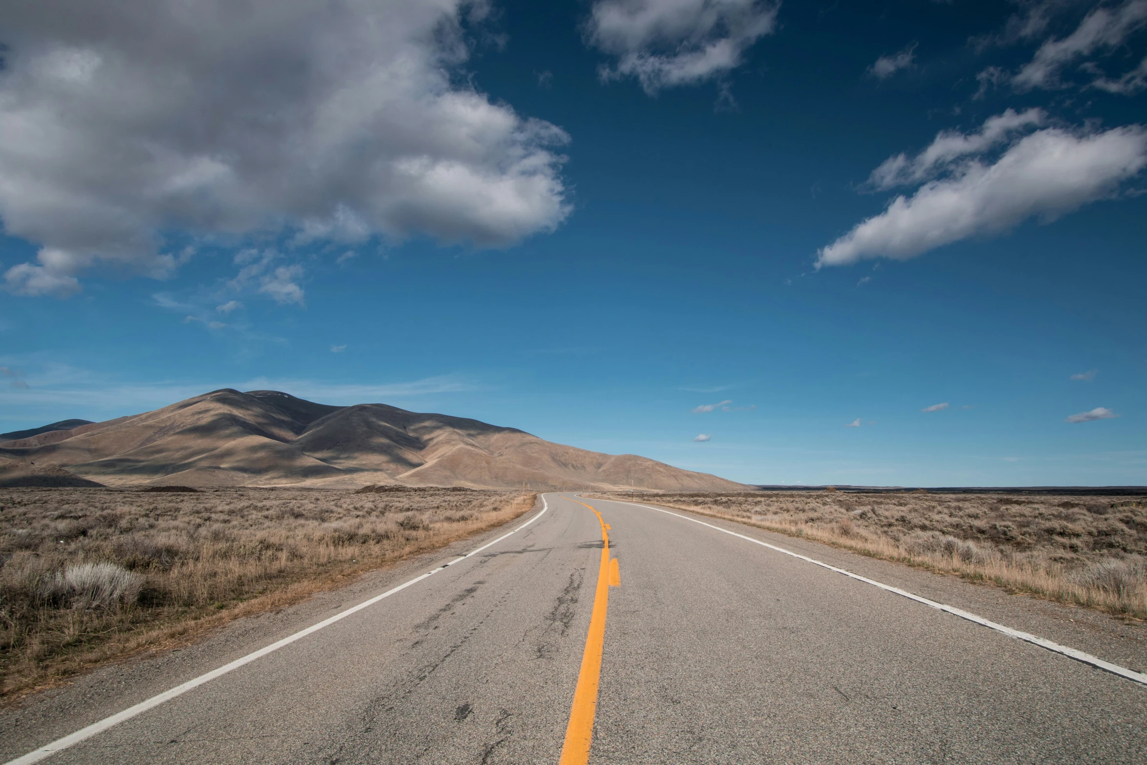 a road with yellow line in the middle between grass and hills