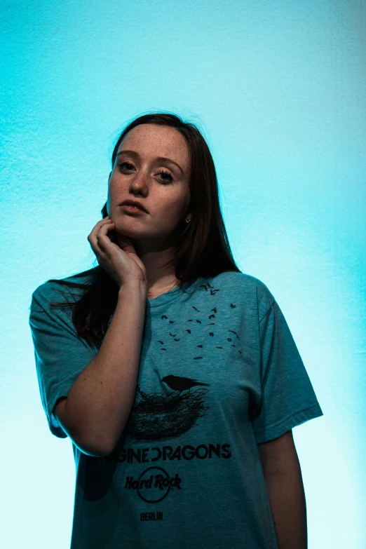 a girl posing in a t - shirt with one of her hands on her chin