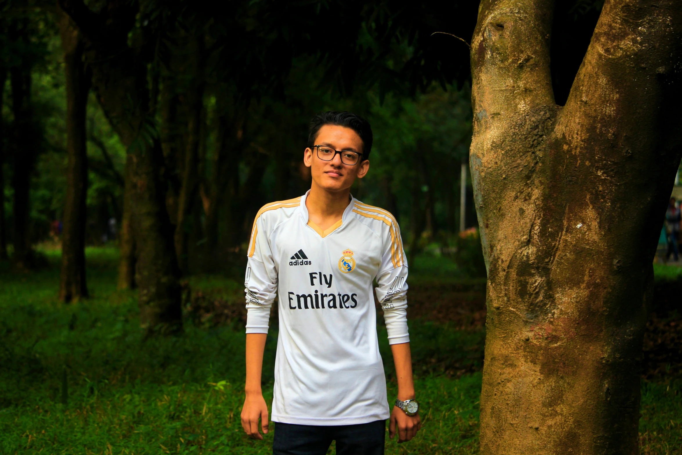 a man in a white and yellow soccer shirt standing next to a tree