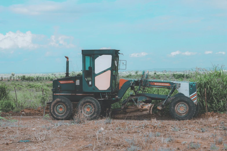 a green tractor on dirt road next to weeds