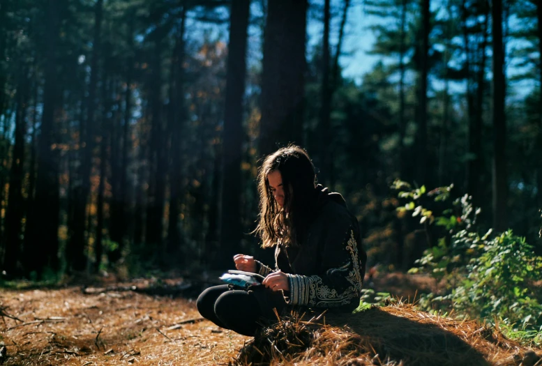 a man is sitting in the woods looking at his cell phone