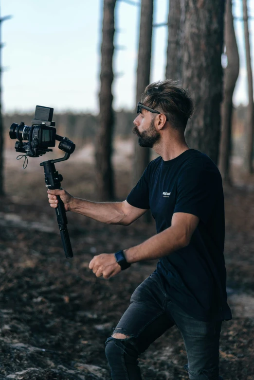 a man holding a video camera with woods behind him