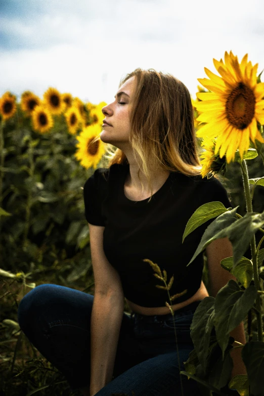 a woman sitting in the middle of a sunflower field