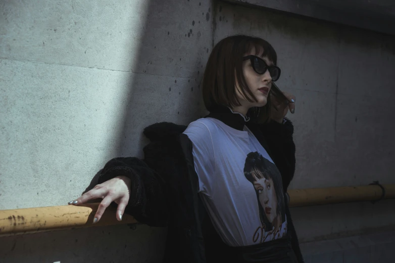 a woman wearing sunglasses leaning against a cement wall