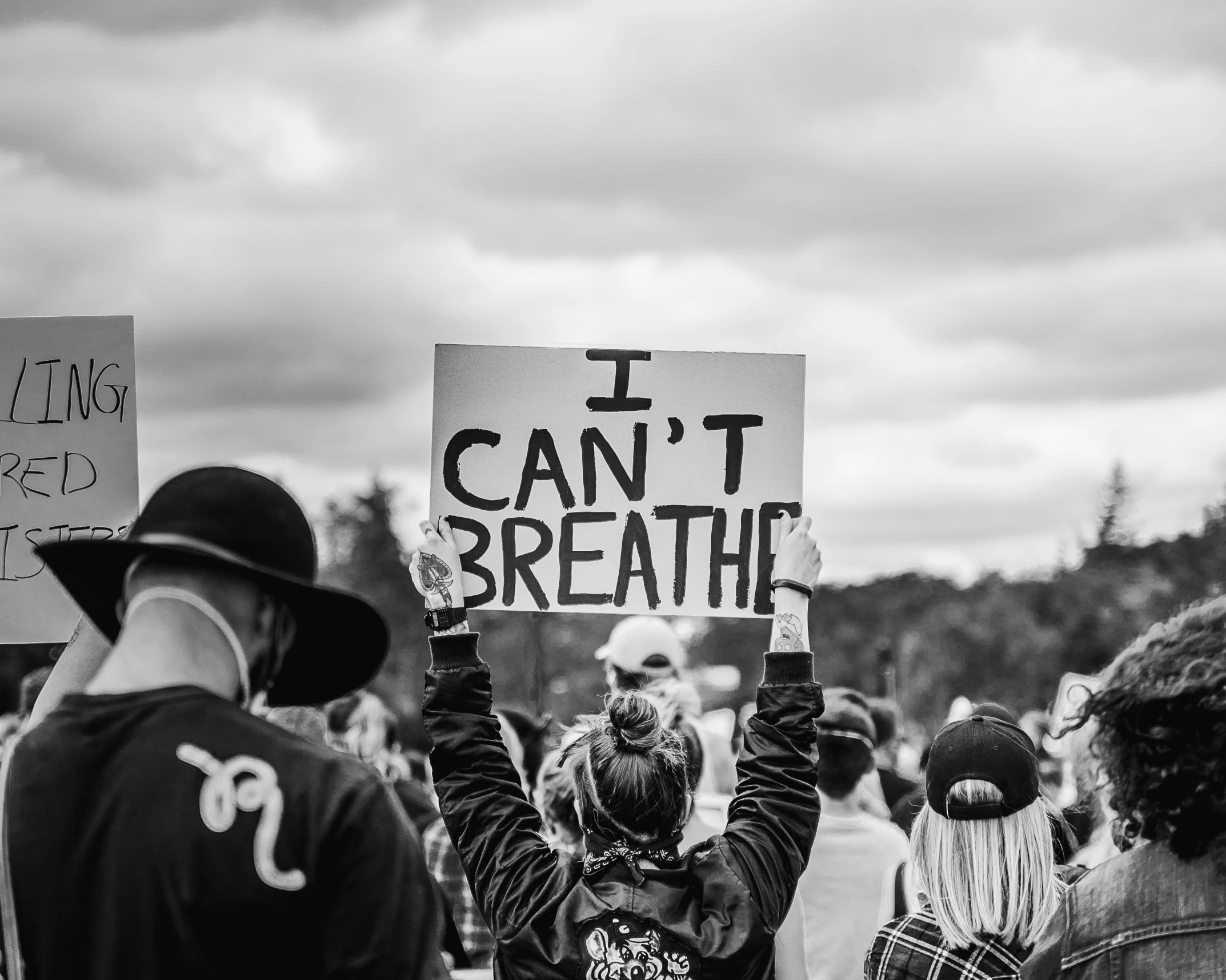 people hold signs at a protest rally on a cloudy day