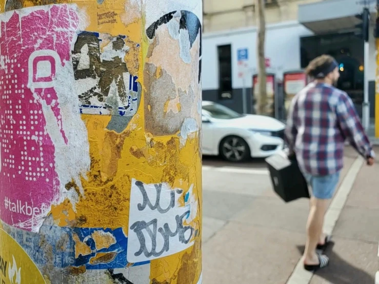 there is a post with stickers on it and a man walking by
