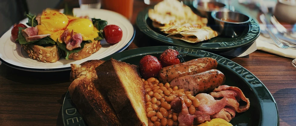 three different plates have sandwiches, beans and fruit on them