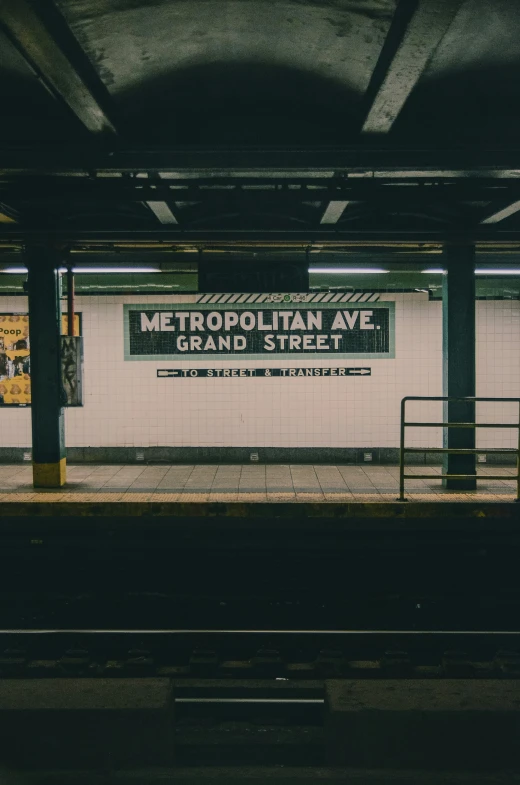 a platform at the subway station with a sign about metropolitan ave and grand street