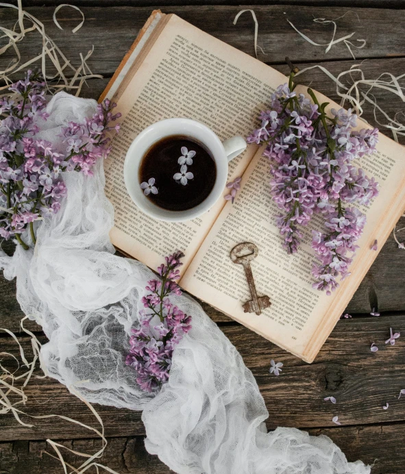 cup of coffee and purple flowers on top of an open book