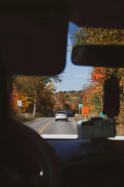 view of a car driving in the road between a stop sign and a street sign