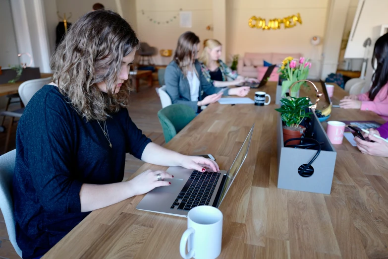 some women are sitting around a long table with laptops and cups