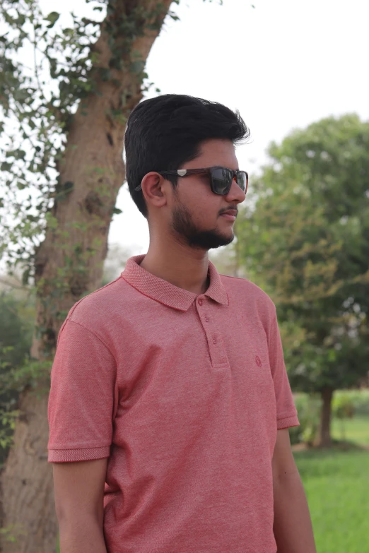 a man with sunglasses stands in front of a tree