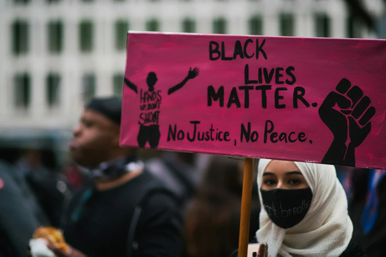 a woman wearing a black mask holding a pink sign