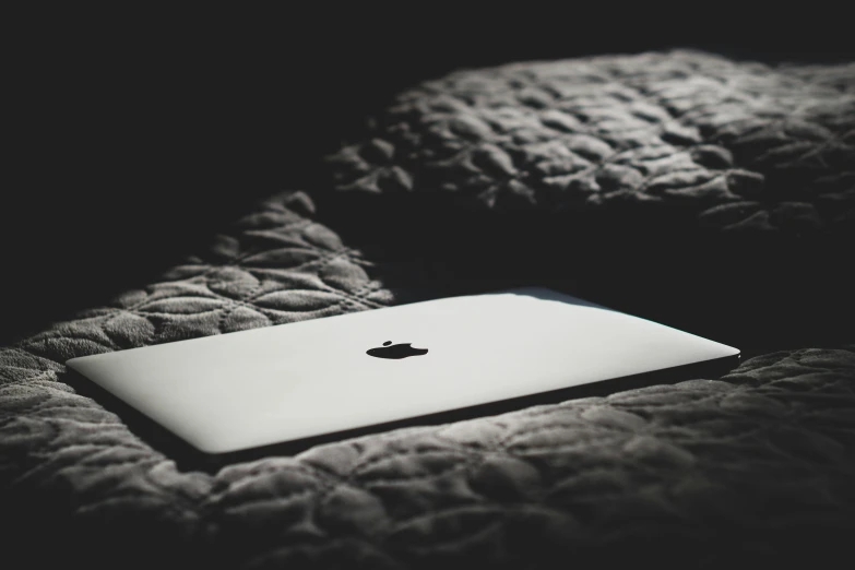 an apple laptop sitting on the bed and black background