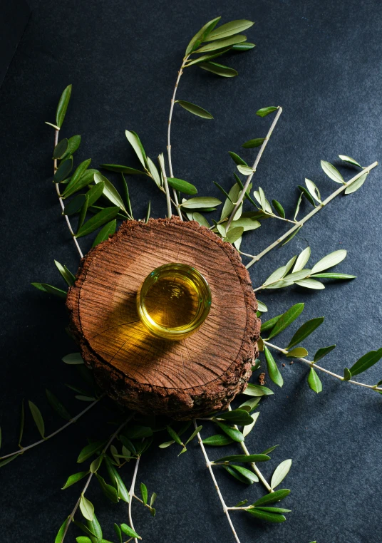 a glass of olive oil surrounded by some leafy nches