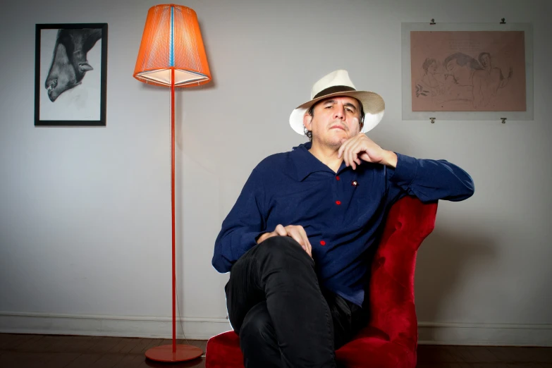 a man wearing a blue shirt and hat sitting in a red chair