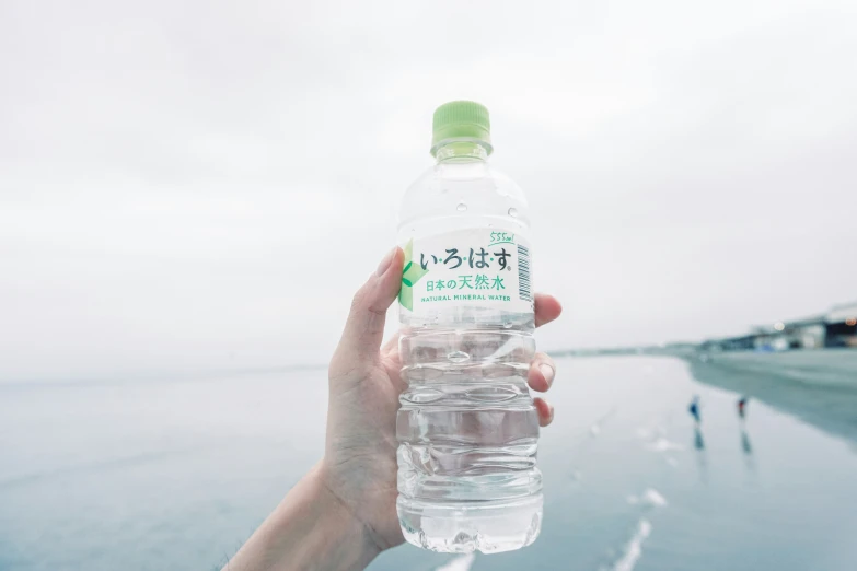 person holding up a bottled water bottle near water way