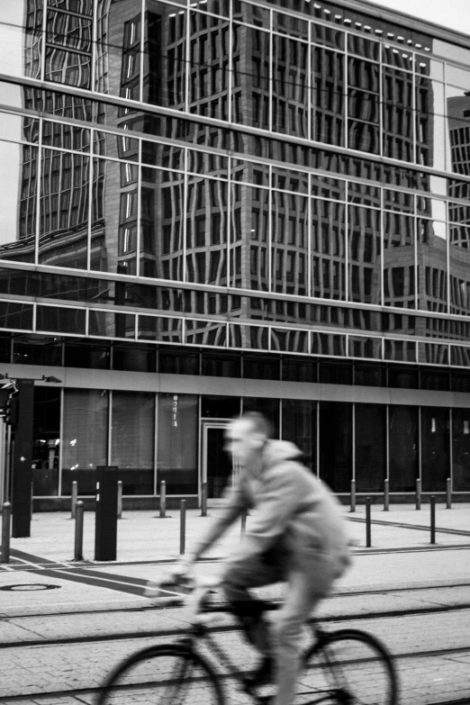 man on bicycle riding past glass building