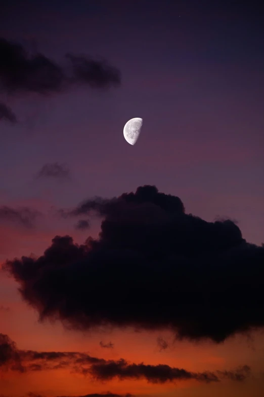 the moon is setting over a city with dark clouds