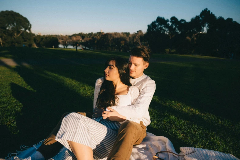 a woman sitting next to a man on top of a grass covered field