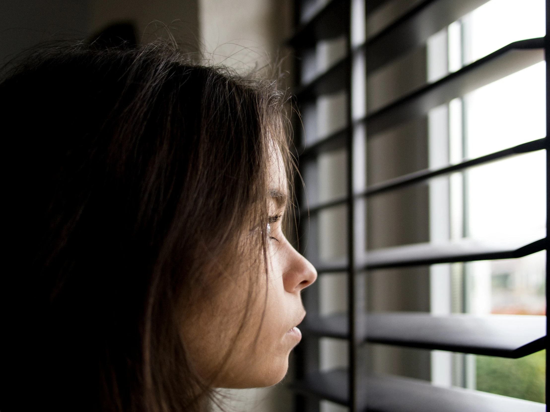 a girl looking out a window with blind open