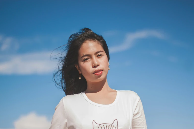 a girl standing on a beach with her hand over her shoulder and the sky in the background