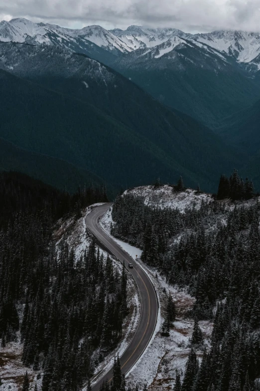 a winding mountain road with trees and snow on the ground