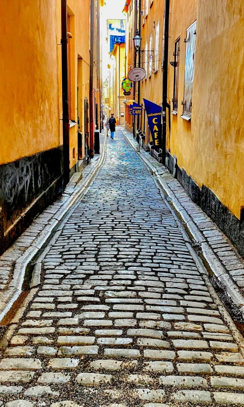 a cobblestone road in a historical area with yellow buildings and people walking along the street