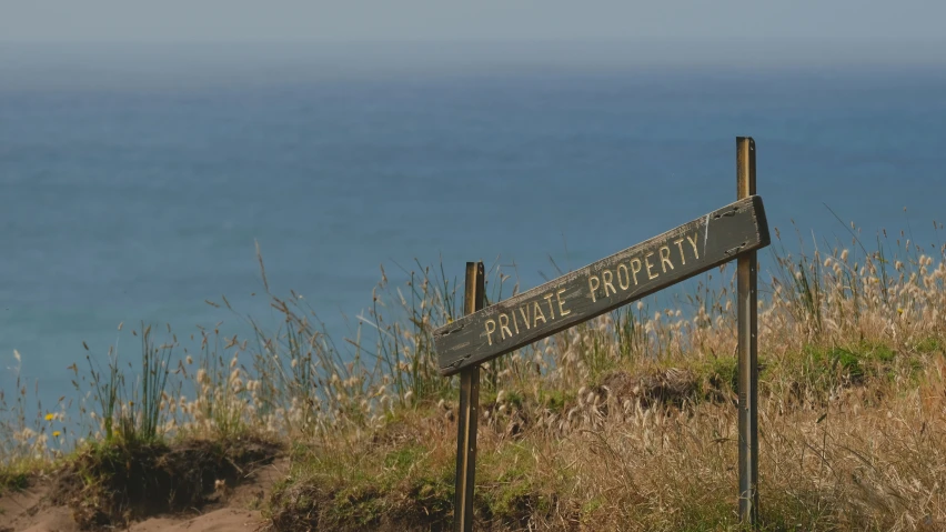 a wooden sign sitting on the side of a cliff overlooking the ocean