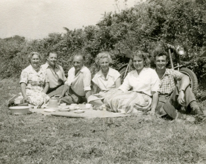 a black and white po of a group of people in the grass with food on a blanket