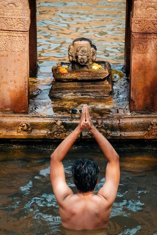 man in water near a statue with one hand raised at the base