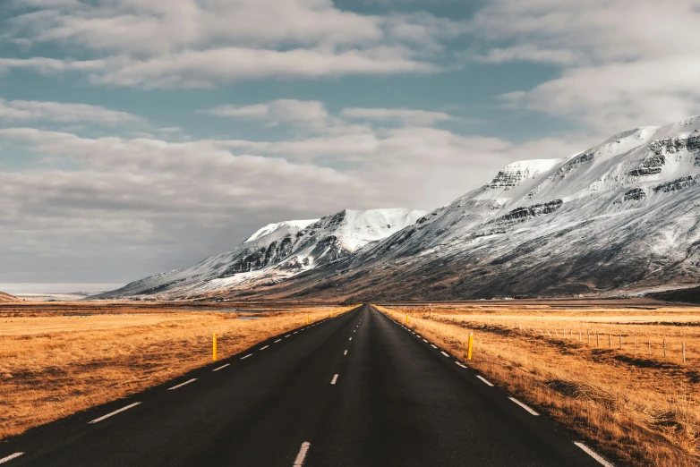 the road is lined with dry grass, brown grass and mountains