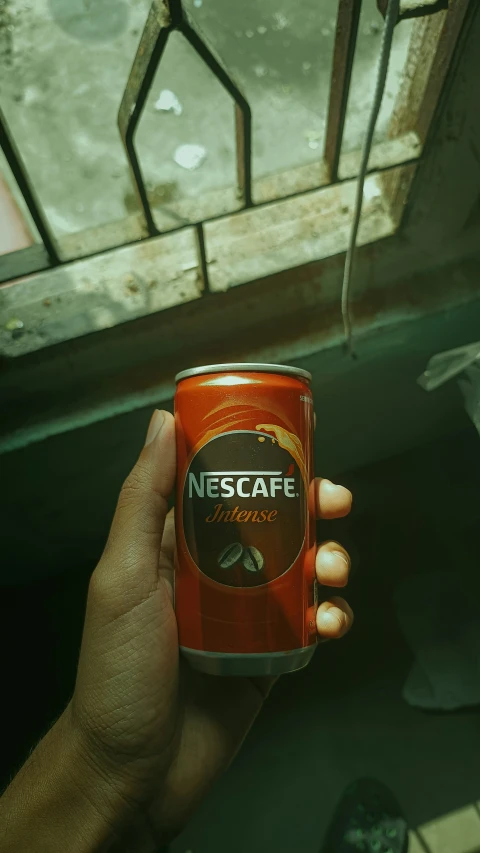 a hand holding an empty can of soda near windows