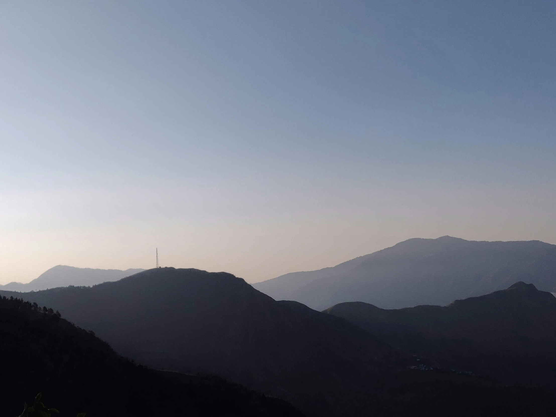 a clock tower is on a hilltop near mountains