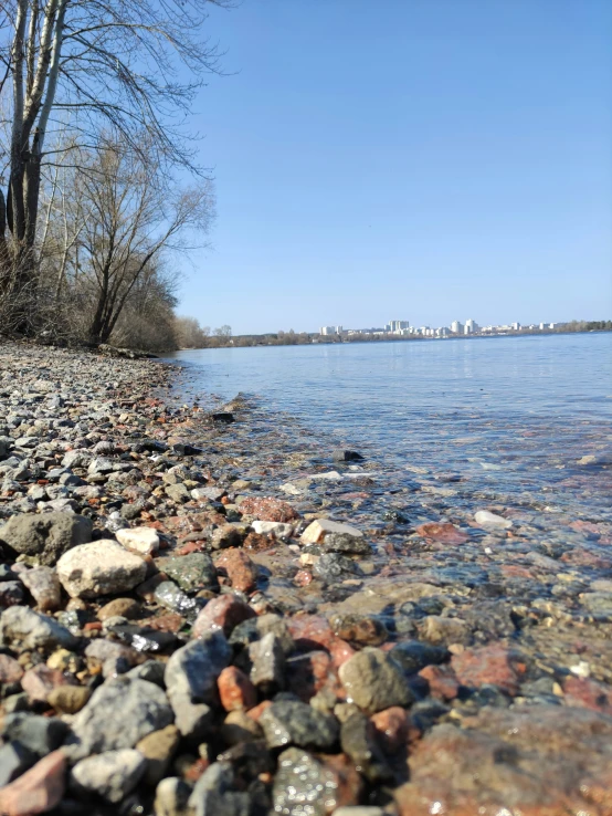 rocks on the shore of a lake with buildings in the distance