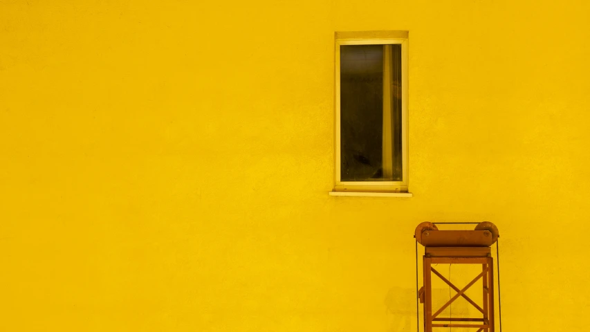 a small wooden chair by a yellow wall with a window