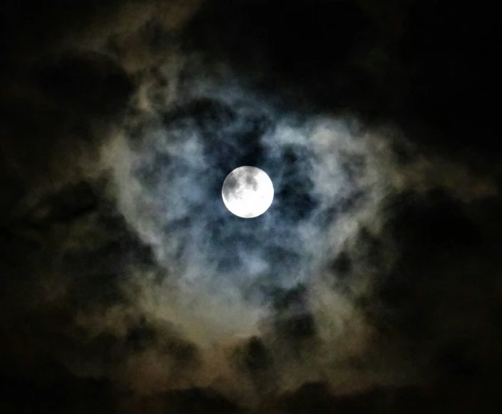 the moon, seen through the clouds, with a dark night sky