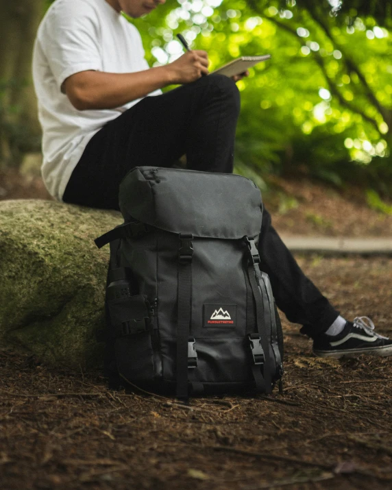 the man is reading the book near his backpack