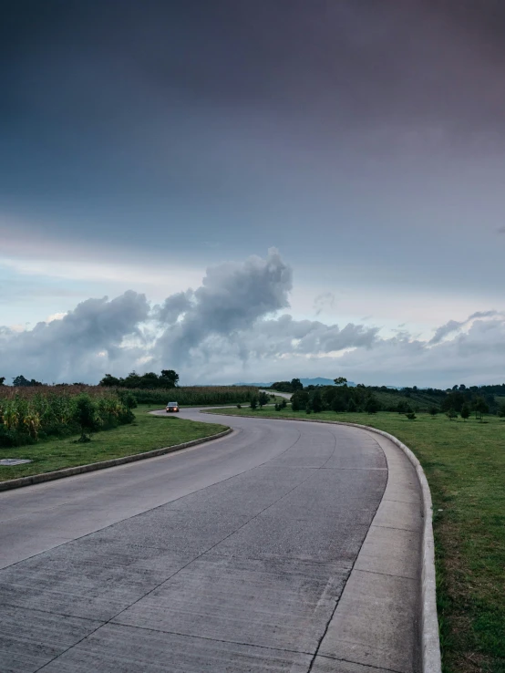 an empty highway on a cloudy day in the middle of a grassy field