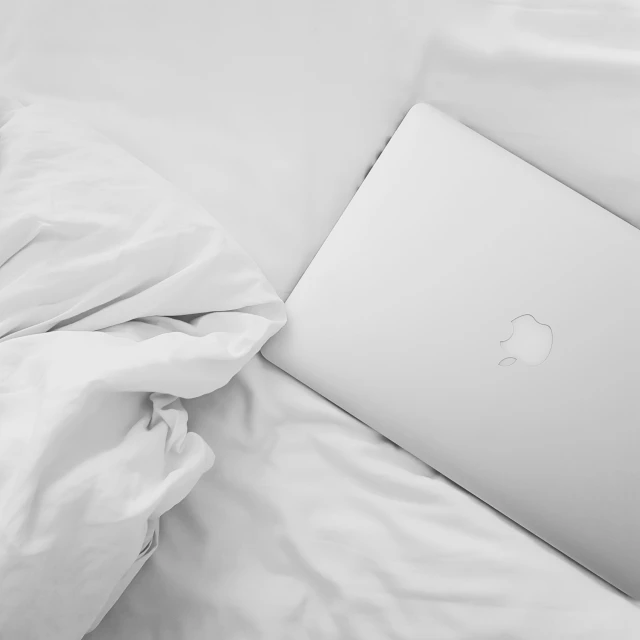 the apple laptop is sitting on the white sheets