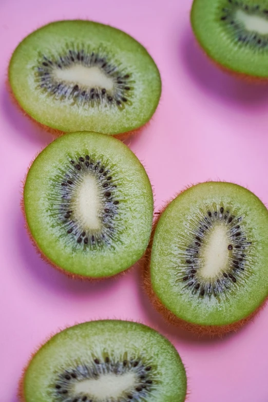 a green kiwi fruit sliced on top of a pink table