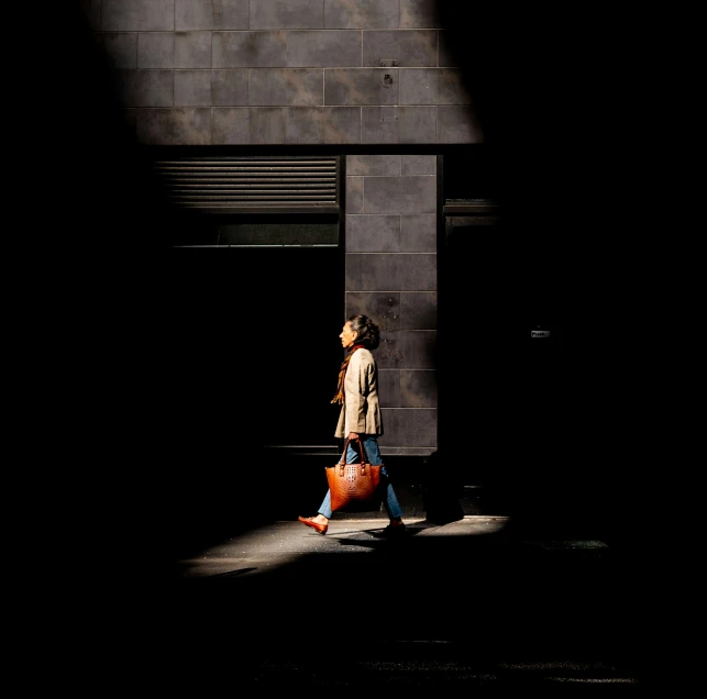 a woman walking past a black building with an orange suitcase