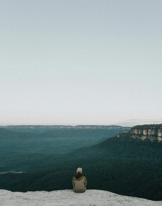 person sitting on cliff looking over water and mountains